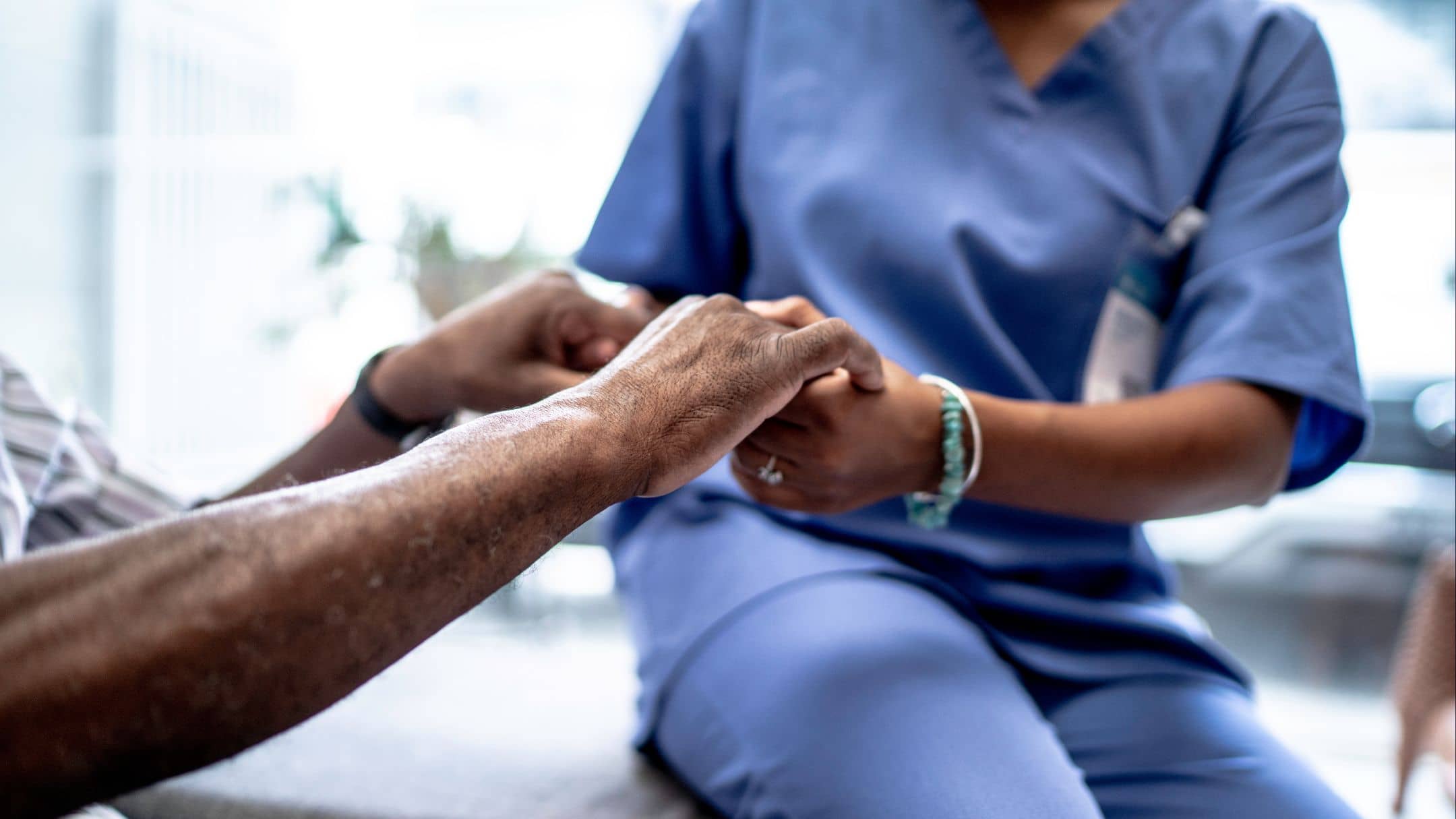 Compassionate hands holding elderly patient's hand